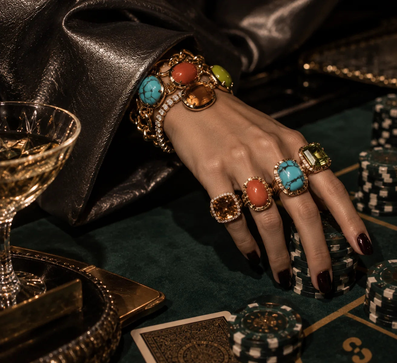 A hand wearing Ilene Joy Rock Candy cocktail rings and a gemstone bracelet at a card table