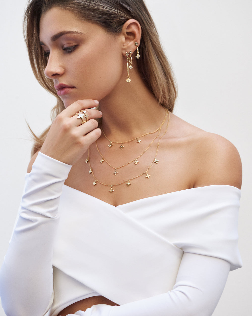 A woman in a white off-the-shoulder top wearing an Ilene Joy gold clover necklace and rings