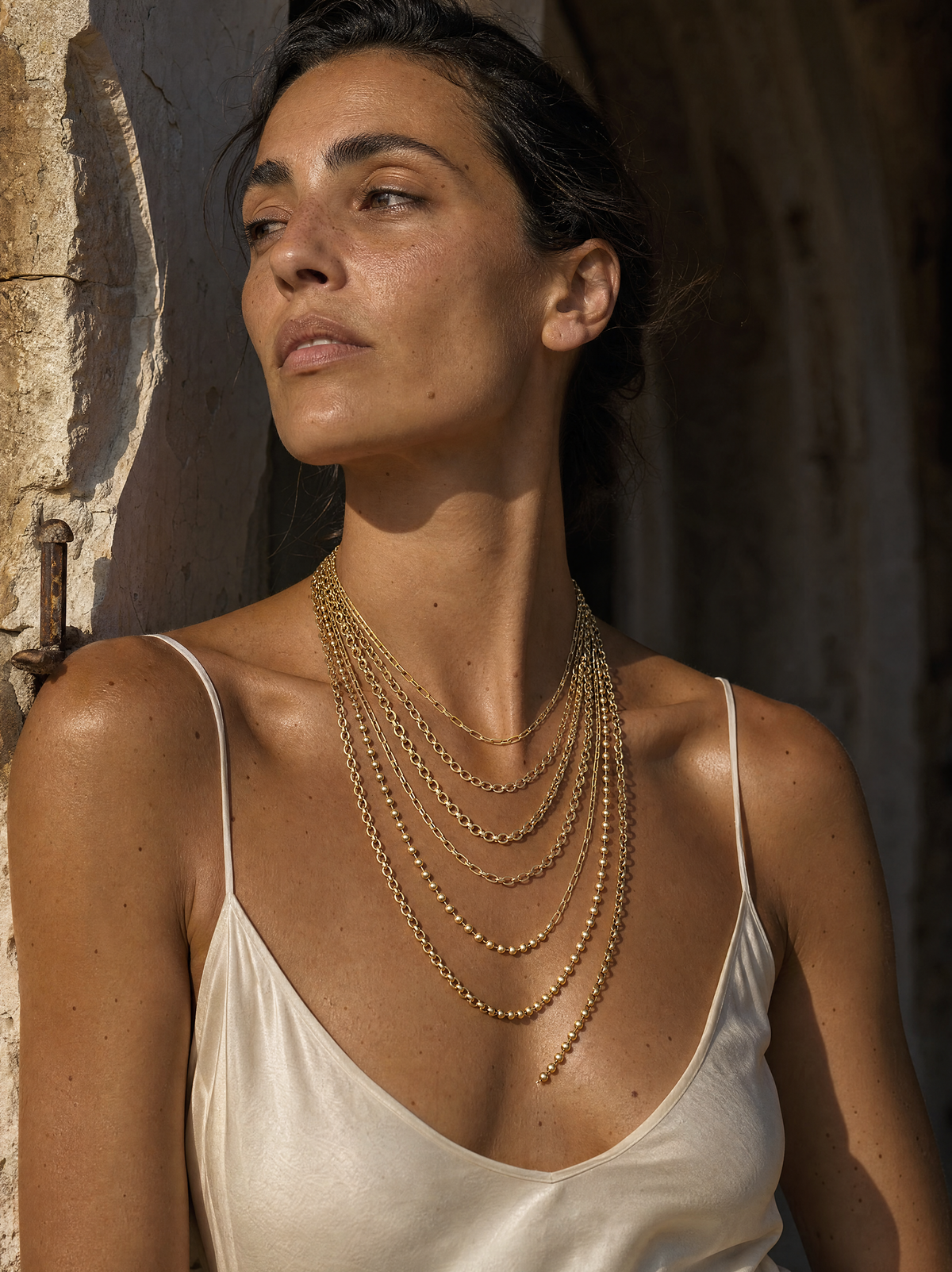 The Reverie multi-strand cascade worn at the throat, seven graduated gold chains against an ivory slip