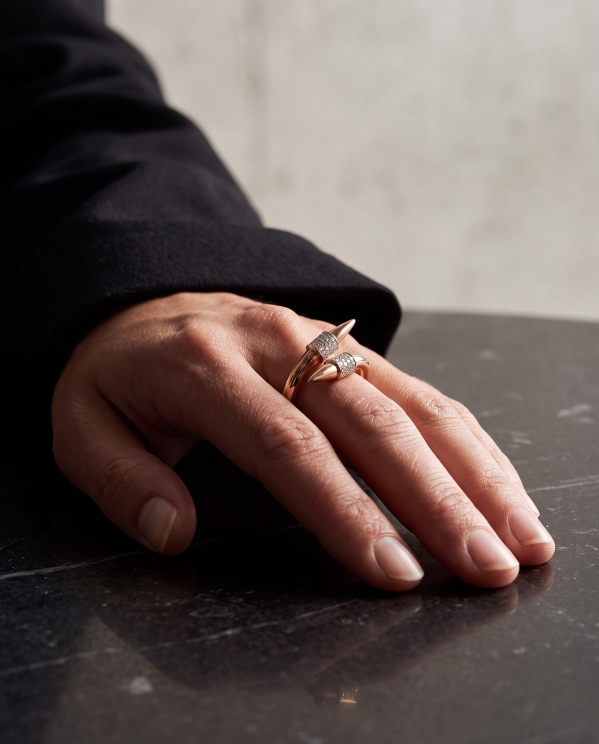 A hand resting on dark stone wearing the Duet Spike ring in rose gold with pave diamond collars